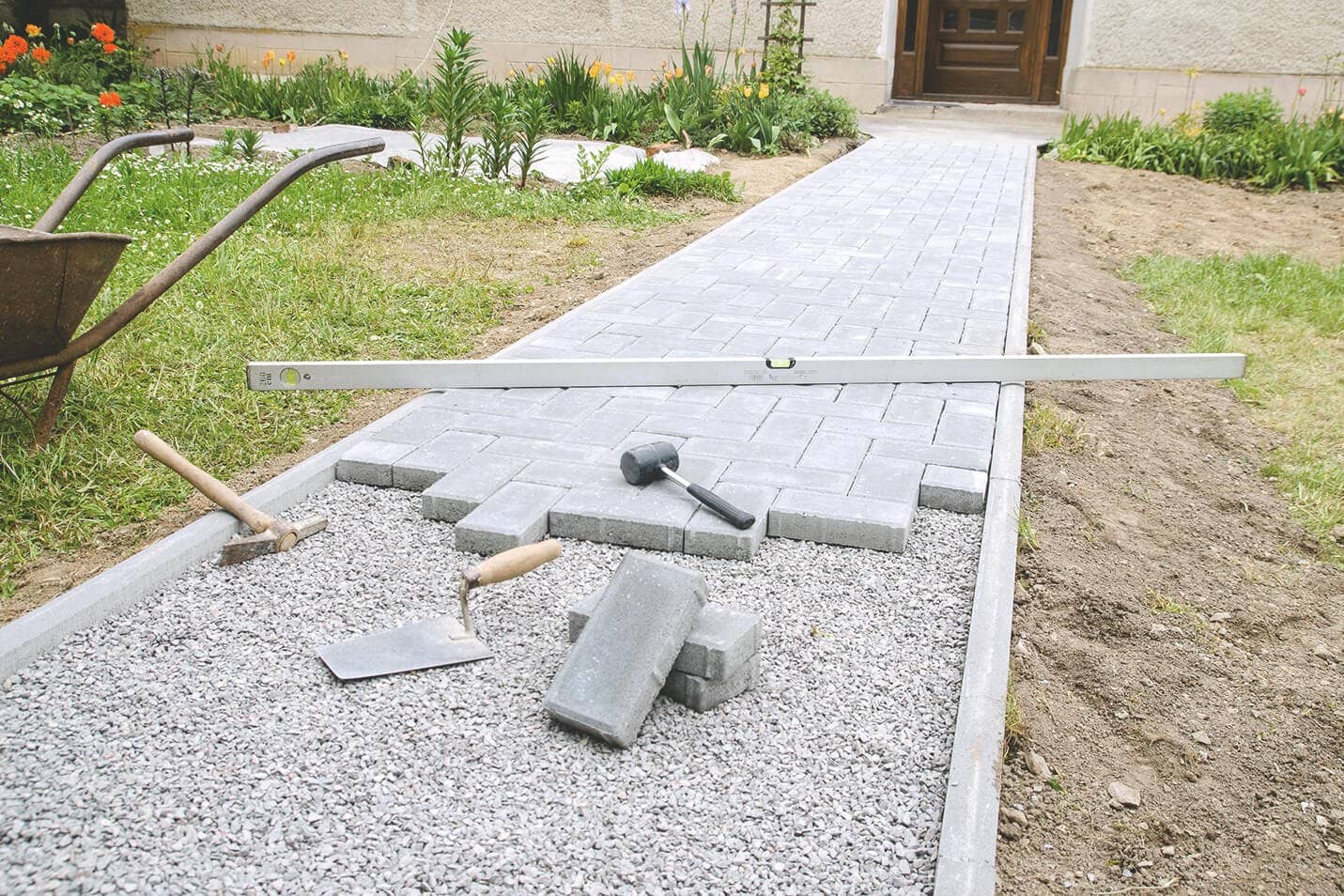 Teilweise fertig verlegter Gartenweg mit Wasserwaage und Werkzeugen im Garten