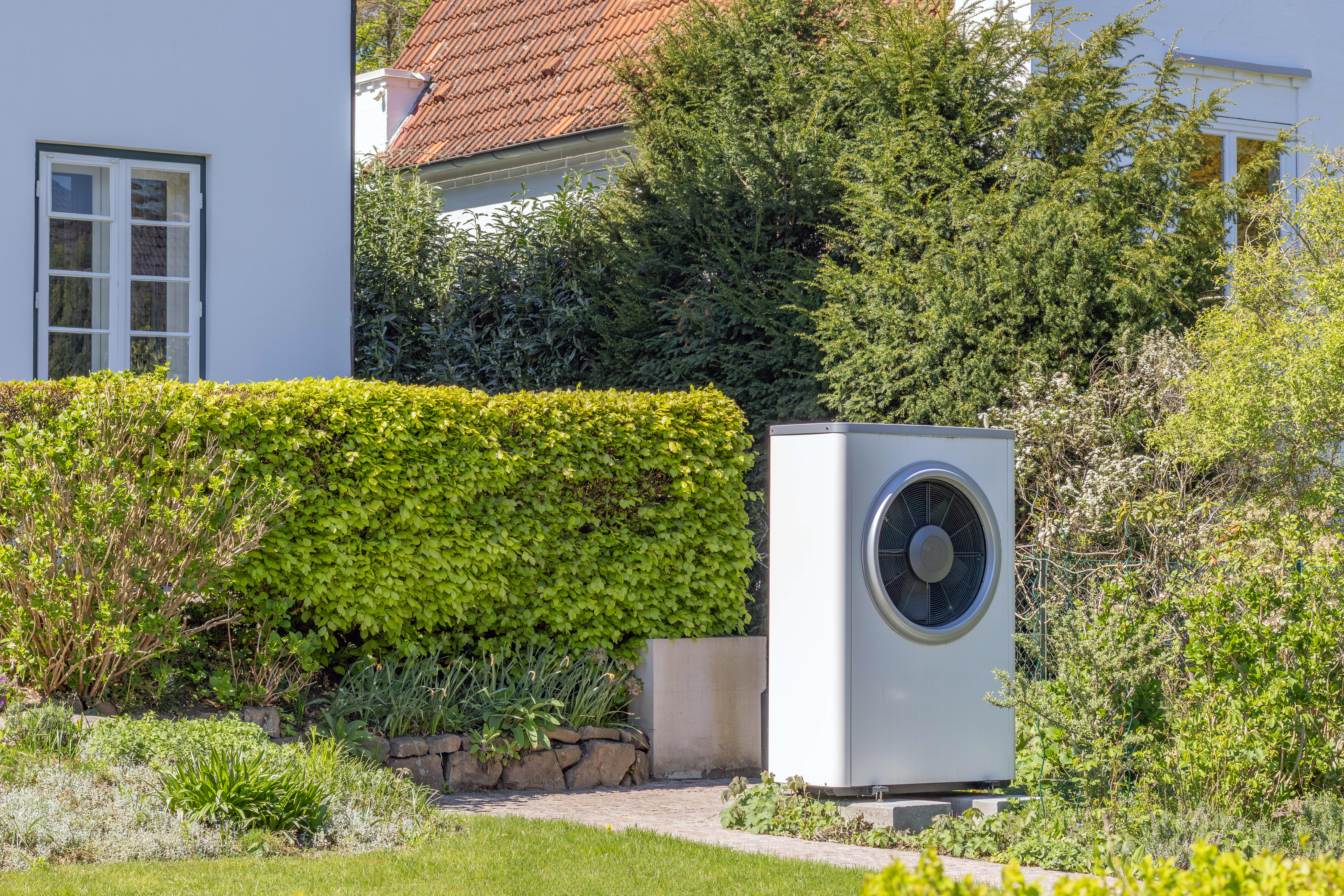 Wärmepumpe im Garten vor einem Haus im Grünen