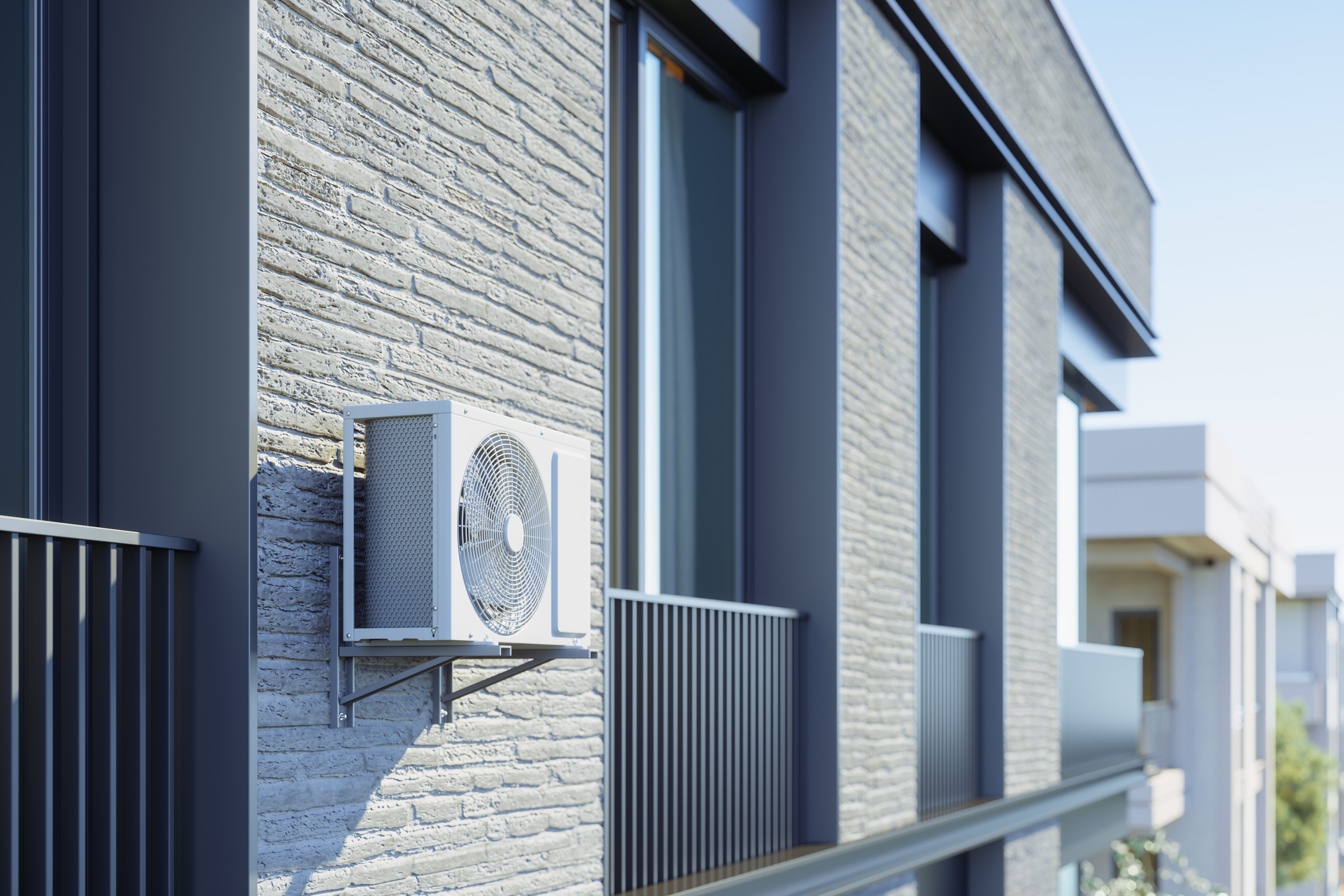 Wärmepumpe an der Fassade eines Mehrfamilienhauses zwischen zwei Balkonen