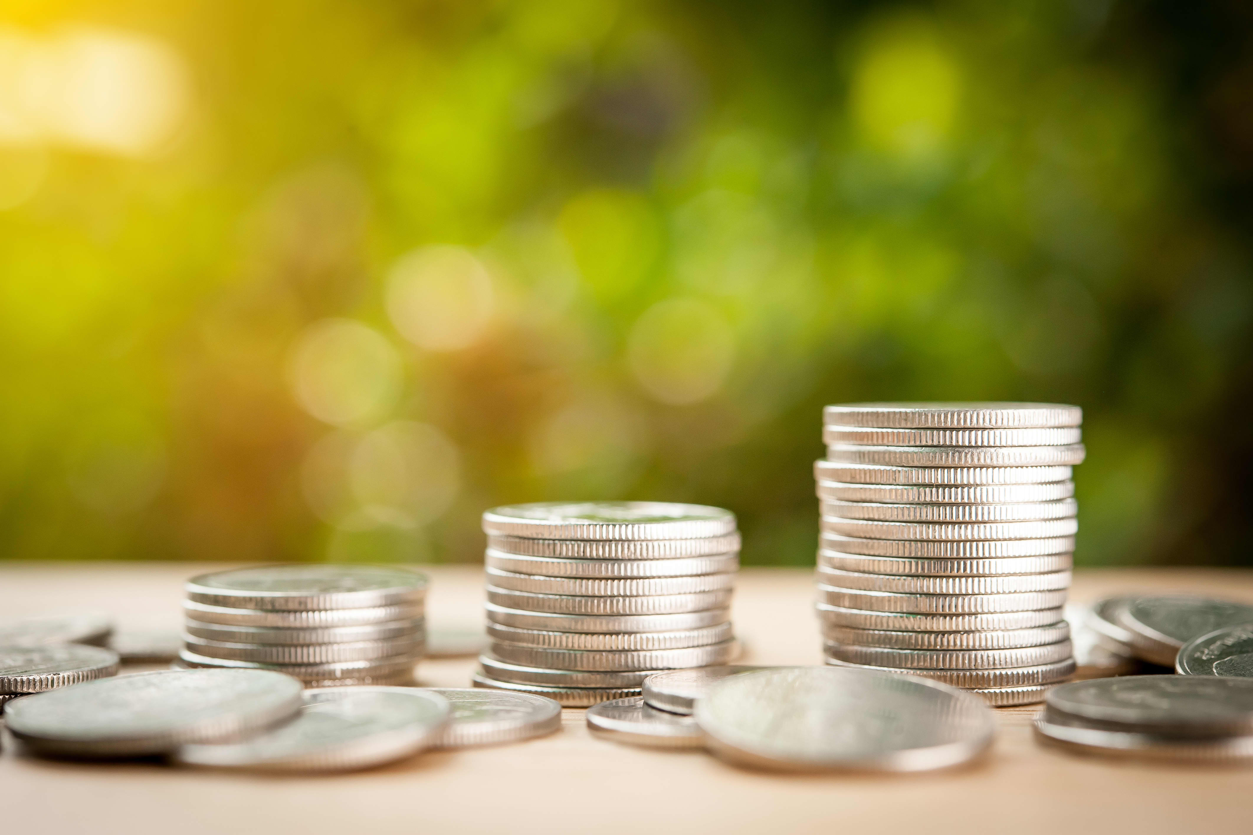 Münzen und Münzstapel in verschiedener Höhe auf braunem Untergrund vor verschwommenem, grünem Hintergrund