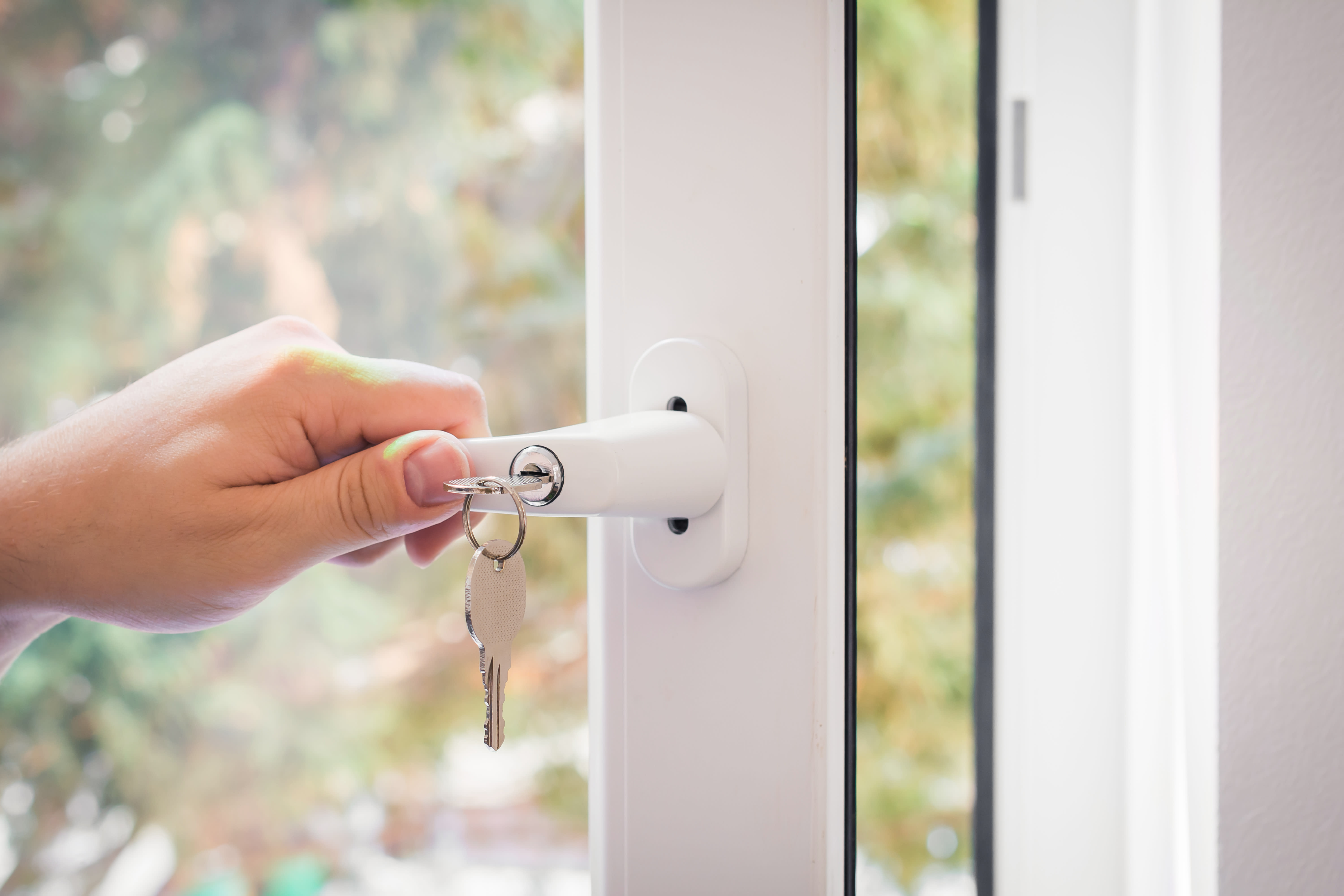 Hand schließt weißen Fenstergriff mit Schlüssel