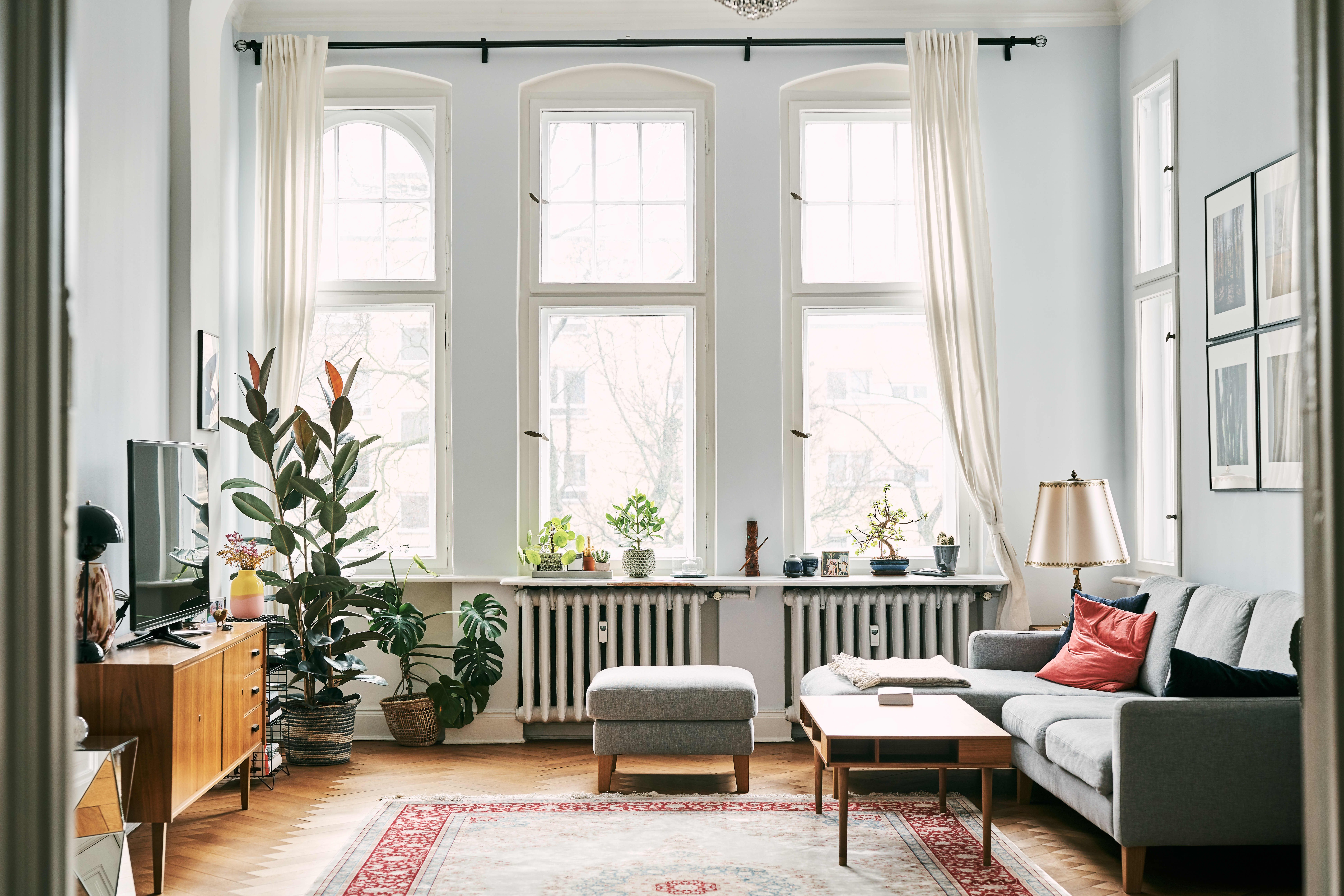 Helles Wohnzimmer mit großen Sprossenfenstern, grauer Couch und Zimmerpflanzen