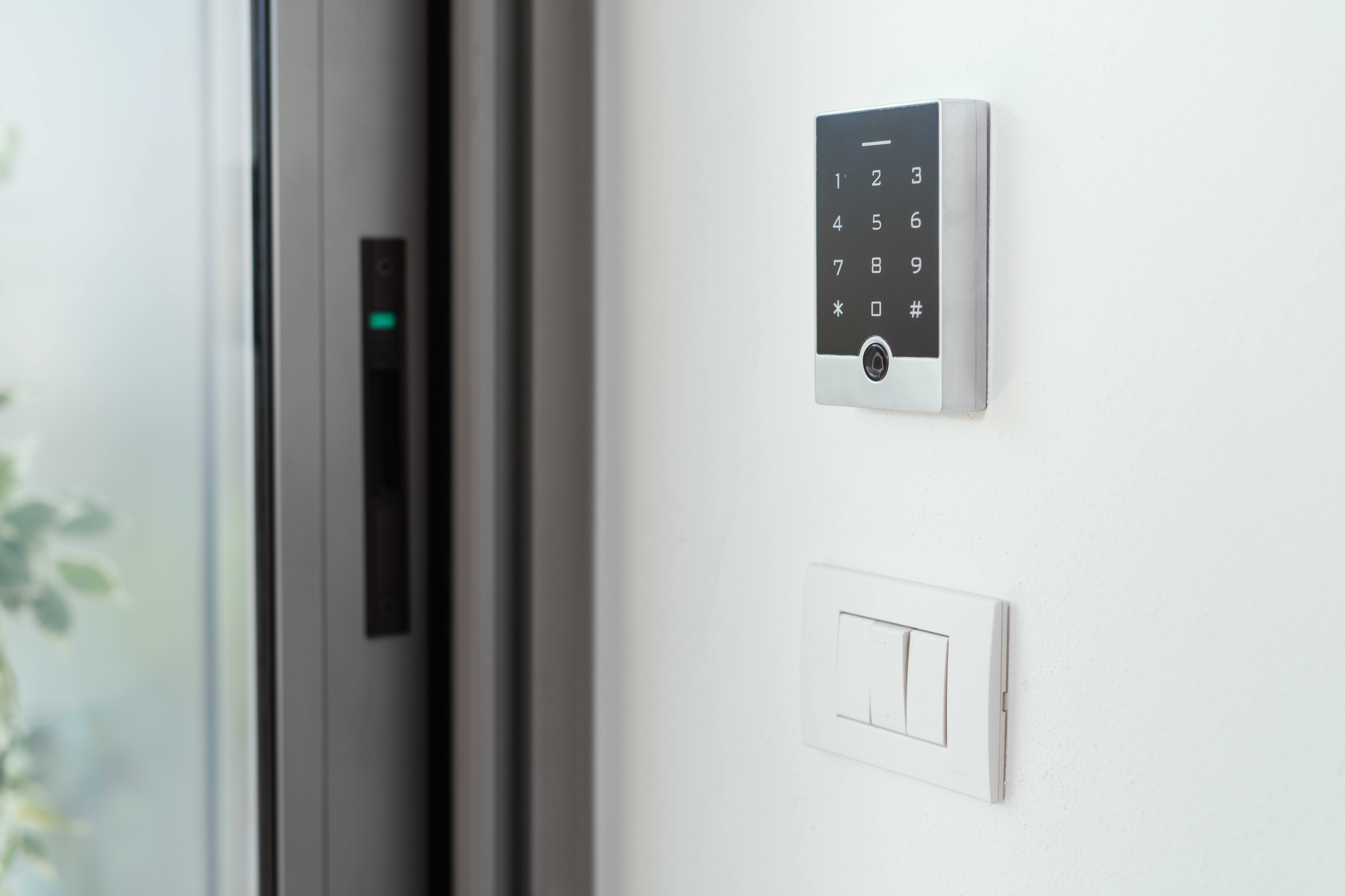 Nummernpad einer Alarmanlage im Inneren eines Hauses über einem Lichtschalter, neben einer modernen Tür