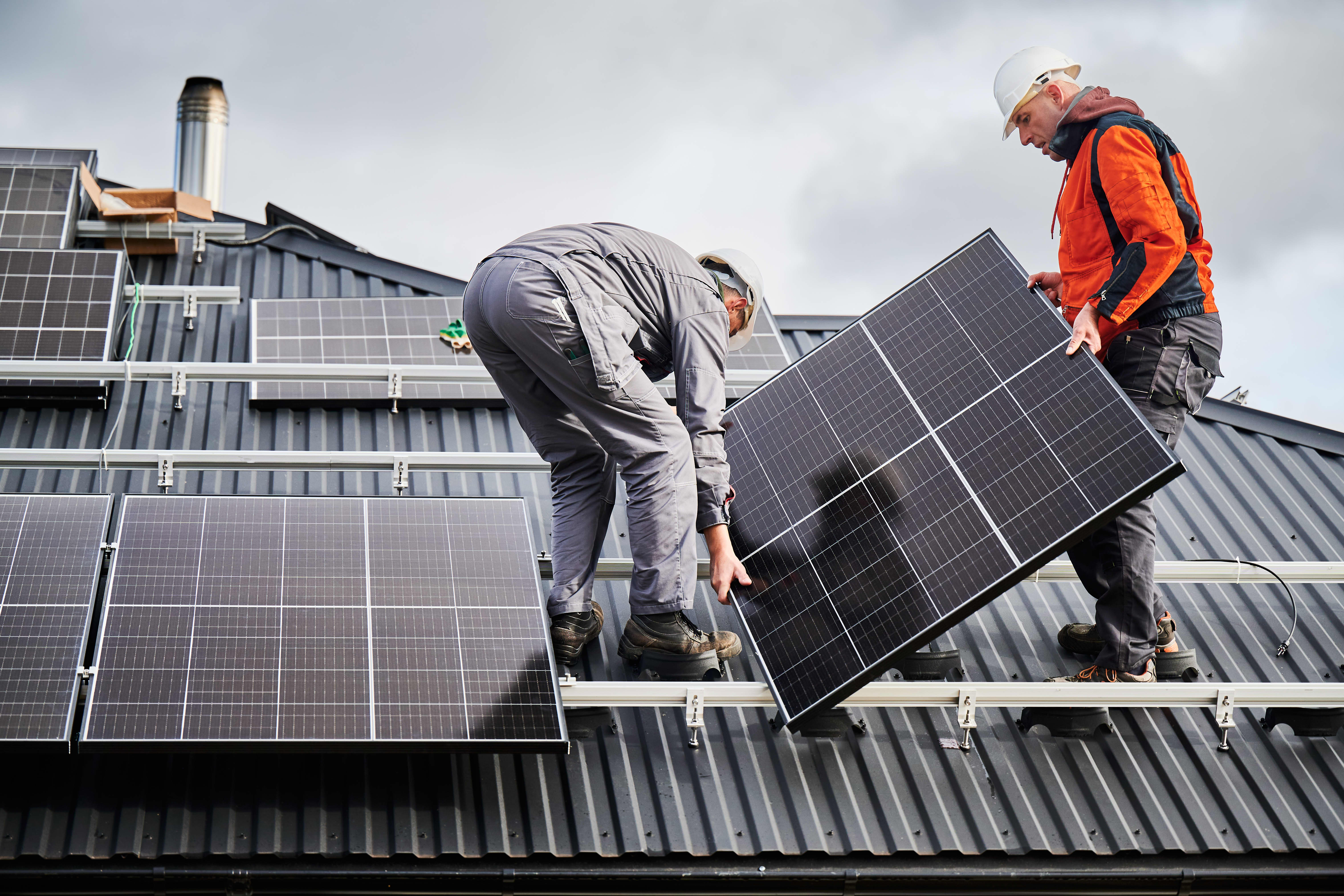 Solarmodule werden auf einem Hausdach von zwei Handwerkern montiert.