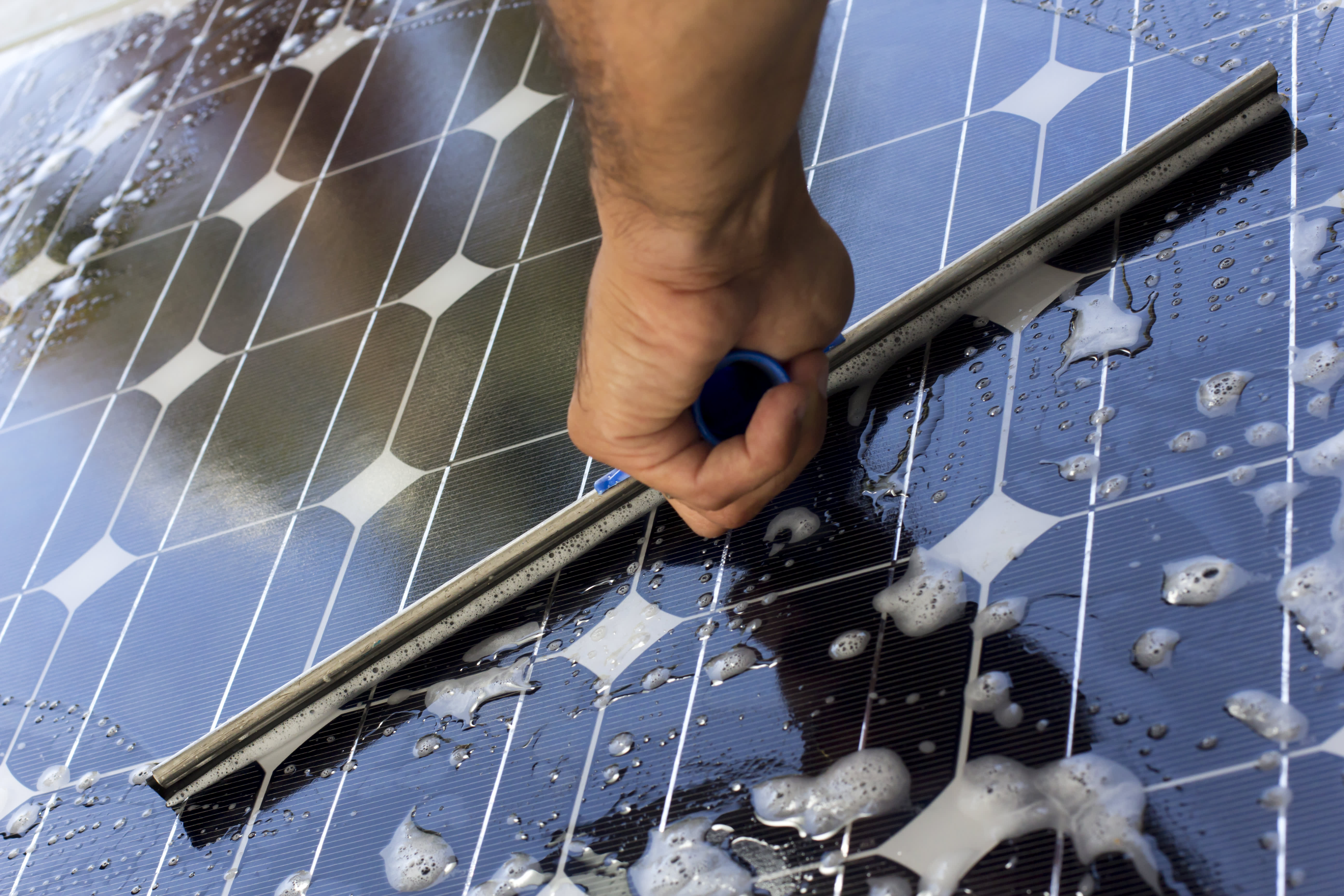 Nahaufnahme einer männlichen Hand, die ein sonnenbeschienenes Solarmodul reinigt