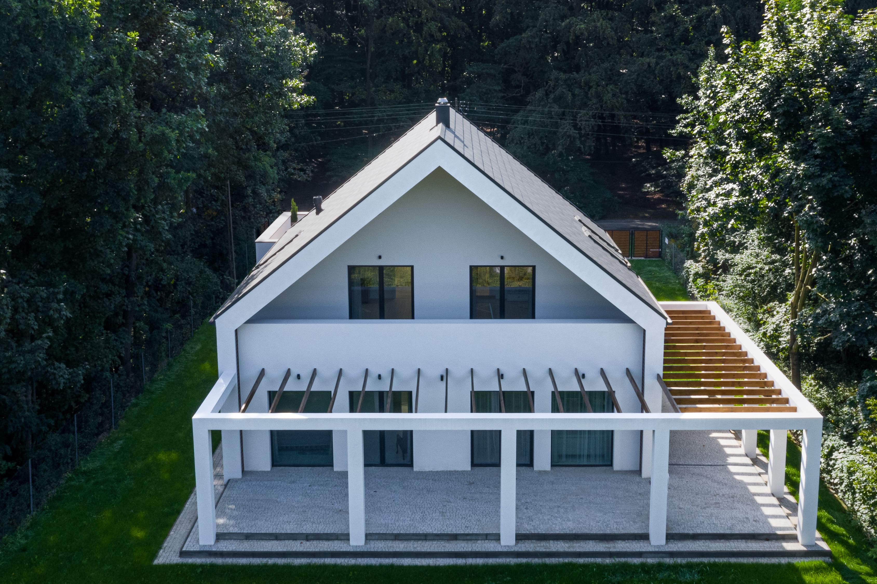 Modernes Haus mit einer L-förmigen Pergola umgeben von hohen Bäumen