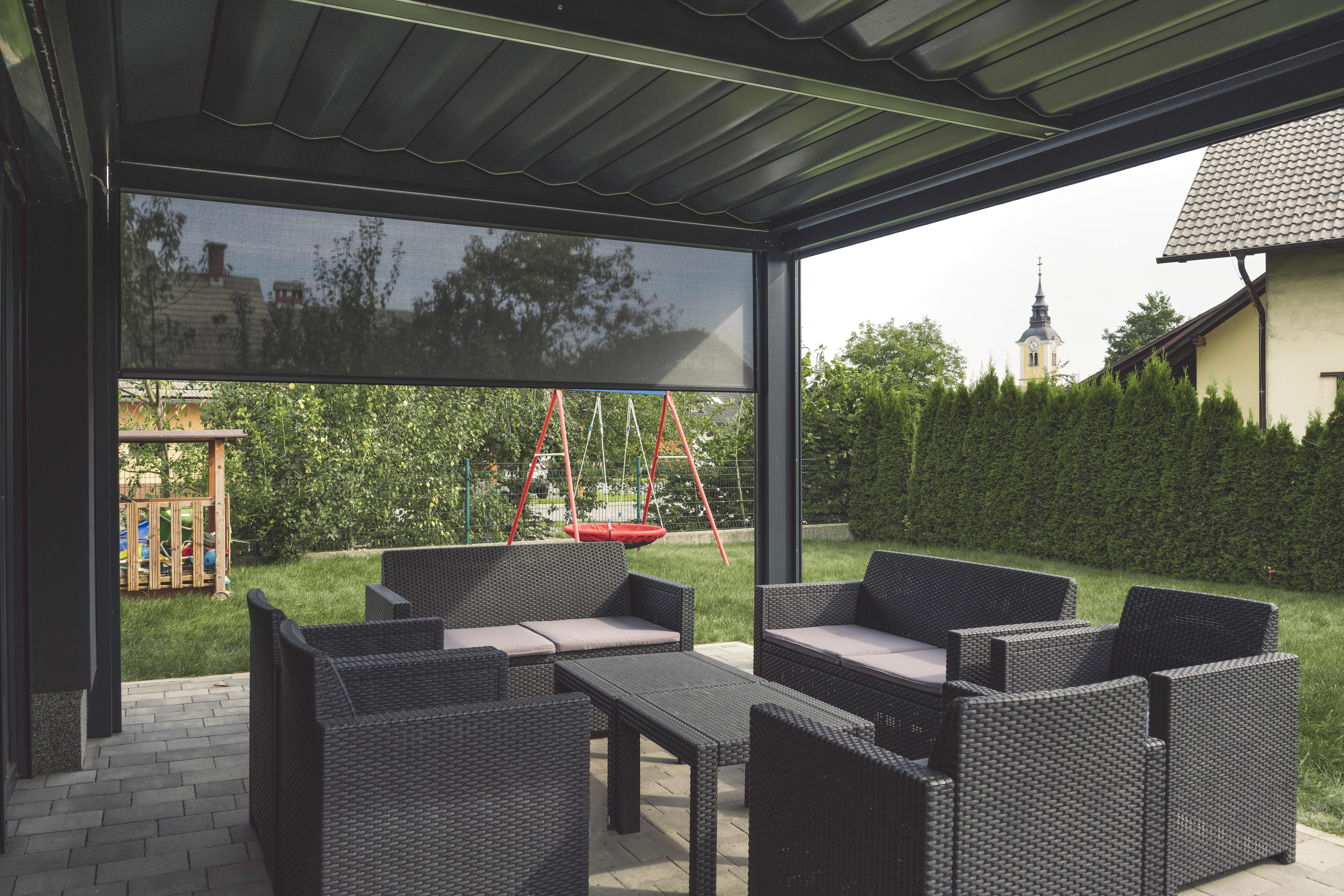 Terrassenüberdachung mit Sitzgruppe und einem halb heruntergefahrenen Seitenrollo