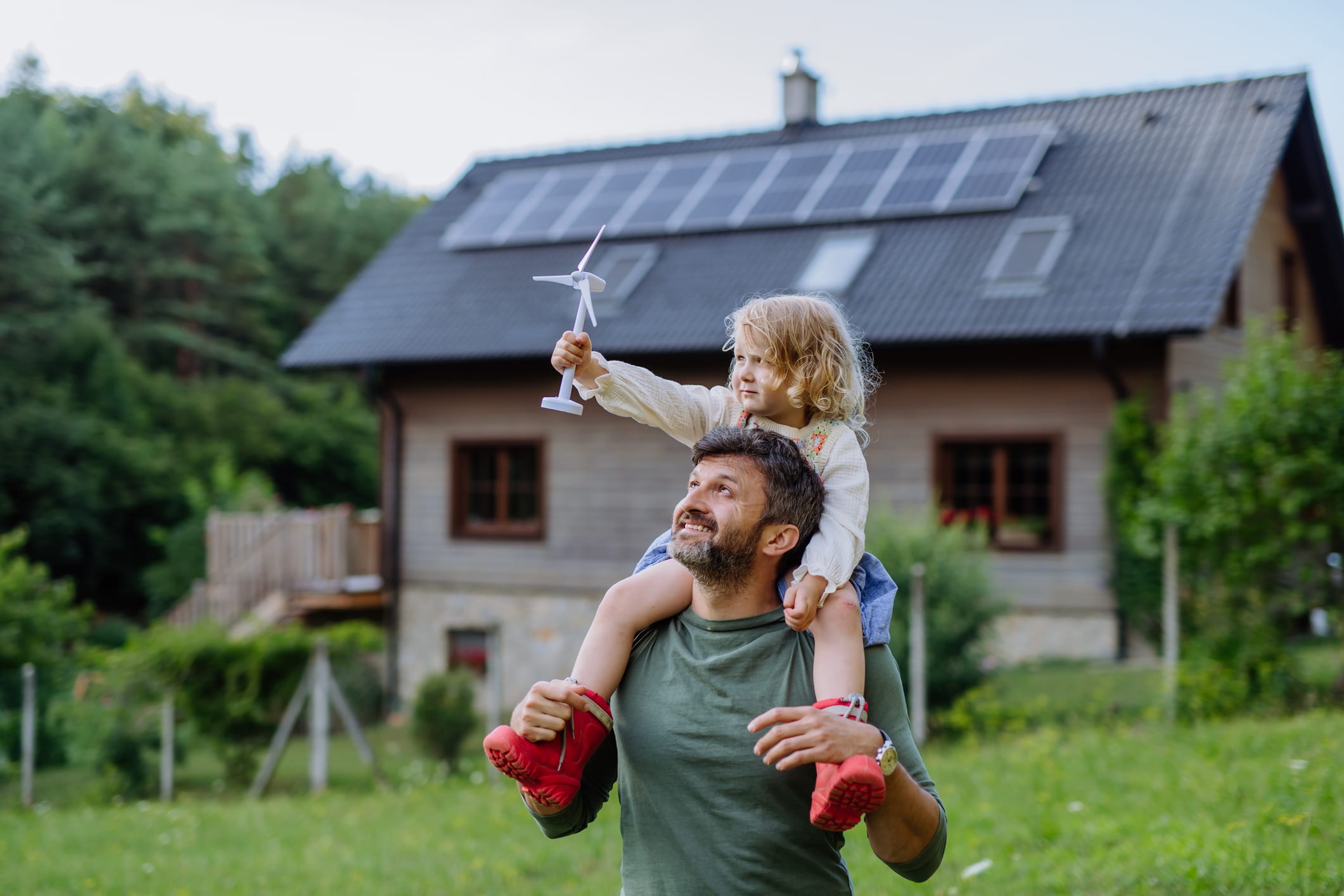 Vater und Tochter vor einem energieeffizientem Einfamilienhaus mit Solardach.
