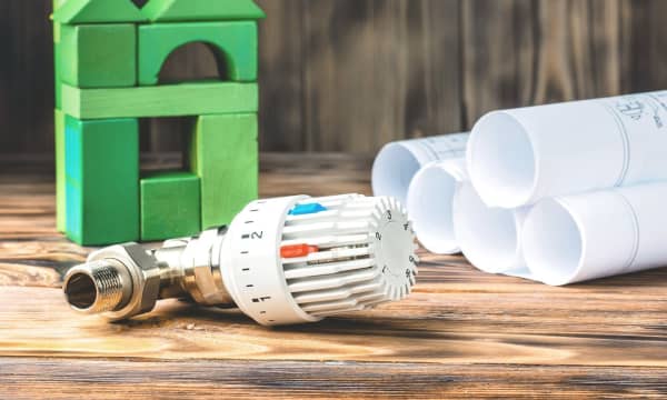 Thermostat neben Bauzeichnungen und grünem Haus