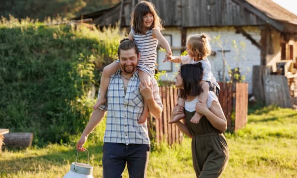 Junge Familie mit Mutter, Vater und zwei Kindern spazieren glücklich vor altem Haus
