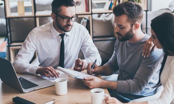 Immobilienmakler und junges Paar am Schreibtisch