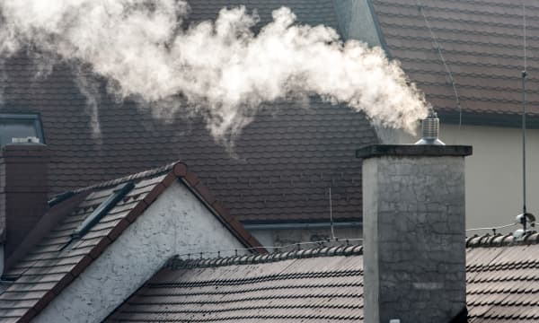 Schornstein mit Rauch vor grauen Wohnhäusern