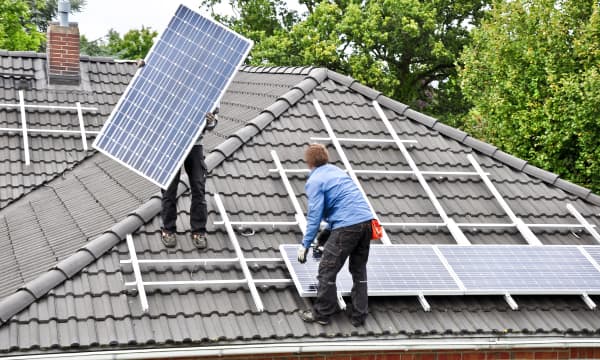 Handwerker montieren zwei Solarpanels auf ein Hausdach