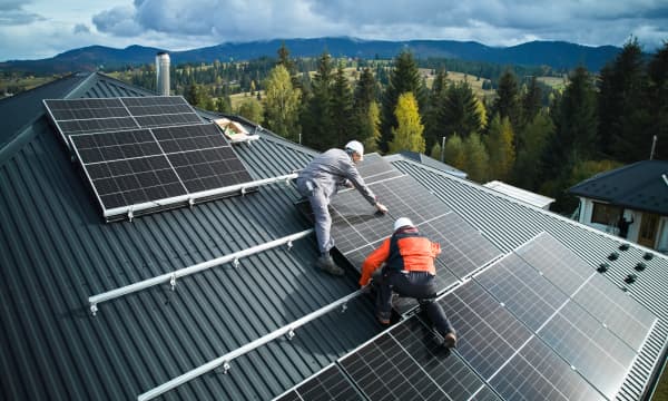 Zwei Installateure errichten eine Solaranlage auf einem Wohnhaus vor schöner Waldkulisse