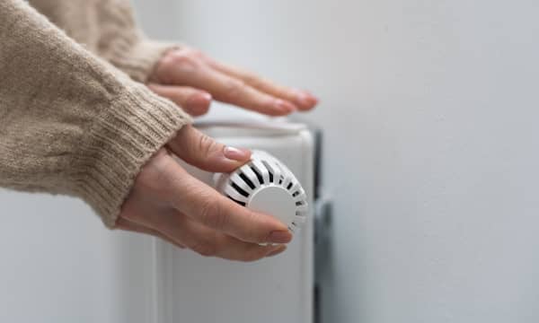 Eine Hand dreht die Heizung auf, die andere liegt auf dem Heizkörper und prüft, ob es warm wird