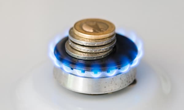 Euromünzen liegen auf einem kleinen Gasbrenner mit blauer Flamme