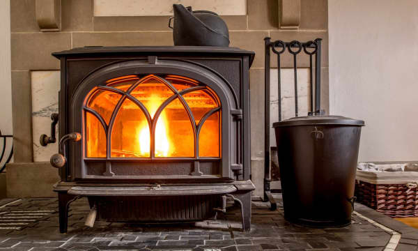 Moderner brennender Kaminofen aus Gusseisen im Wohnraum mit gusseisernem Teekessel zur Luftbefeuchtung oben auf dem Ofen
