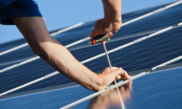 Zwei Hände montieren Solarmodule auf einem Dach