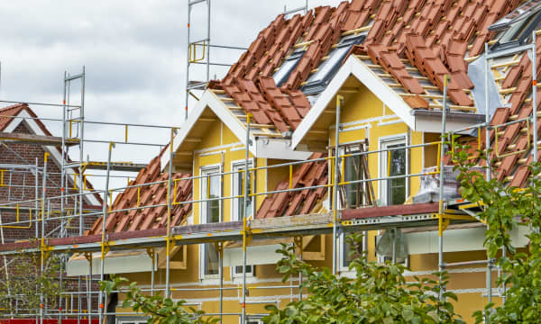 Gerüst an Wohnhaus mit gelber Fassade, dessen Dach neu gedeckt werden soll