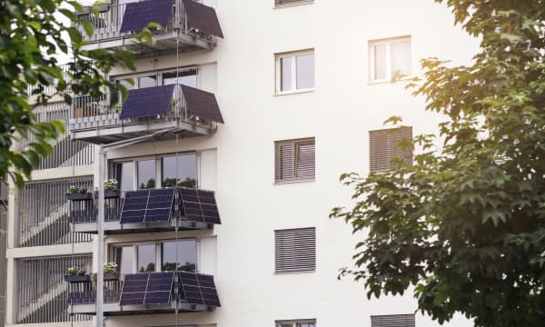Mehrfamilienhaus mit heller Fassade und Balkonen, an denen jeweils mehrere Solarmodule installiert sind