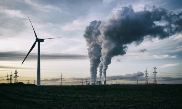 Windrad vor bewölktem Himmel, im Hintergrund Strommasten und ein Kraftwerk