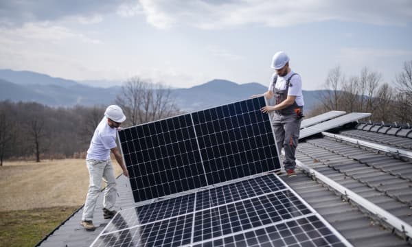 Zwei Installateure montieren ein Solarmodul auf ein Hausdach.
