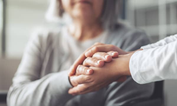 Seniorin und jüngere Person halten sich die Hände