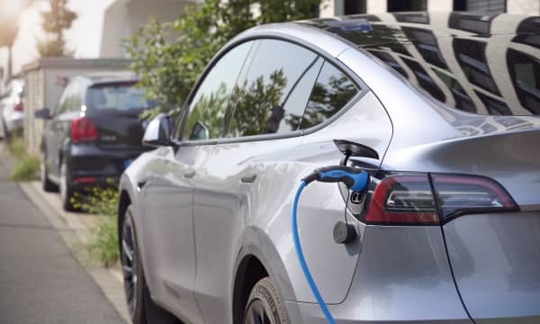 Silbernes Elektroauto am Straßenrand mit eingestecktem Ladestecker
