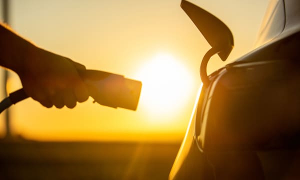 Person steckt bei Sonnenuntergang einen Ladestecker in ein E-Auto