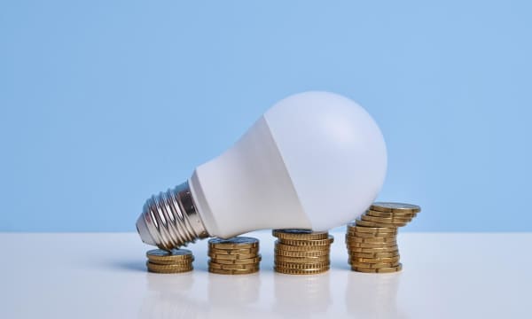 Glühbirne auf aufgetürmten Münzen simuliert ein Wachstumsdiagramm
und verdeutlicht die steigenden Strompreise