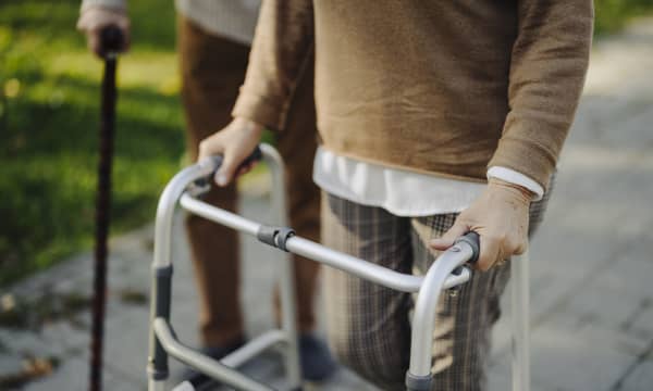 Senior und Seniorin mit Gehhilfe auf gepflastertem Weg