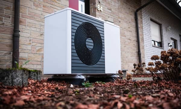 Luftwärmepumpe im Herbst vor einem Wohnhaus mit hellbrauner Steinfassade