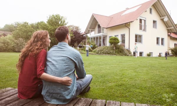 Junges Paar mit Kind im Garten vor einem Einfamilienhaus