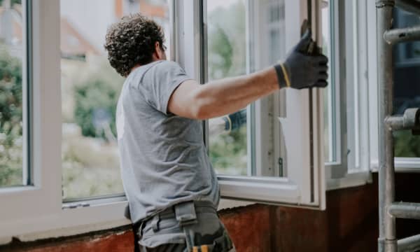 Handwerker hängt den Flügel eines Fensters in einem sanierungsbedürftigen Wohnraum aus