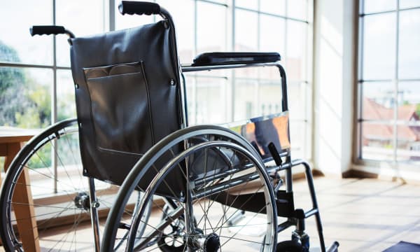 Rollstuhl in einem leeren, hellen Raum mit bodentiefen Fenstern