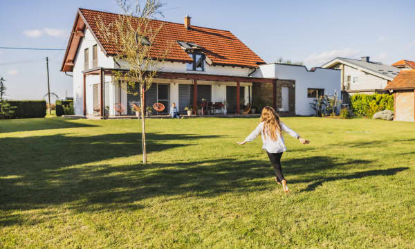 Mädchen rennt mit ausgebreiteten Armen durch den Garten aufs Wohnhaus zu