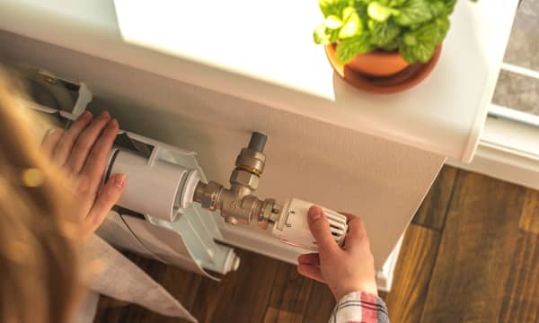 Person dreht das Thermostat eines Heizkörpers