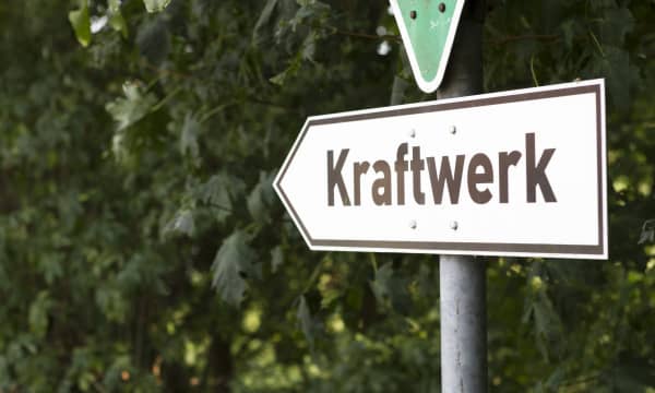 Richtungsweisendes Schild mit der Aufschrift Kraftwerk vor grünen Büschen