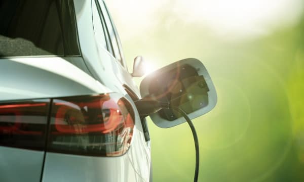Weißes Elektroauto vor grünem Hintergrund wird geladen