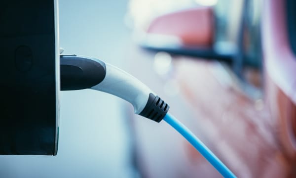 Ladestecker an Wallbox mit verschwommenem Fahrzeug im Hintergrund