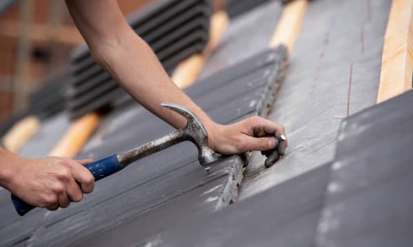 Nahaufnahme eines Arbeiters mit Hammer und Nagel in den Händen, der ein Dach deckt