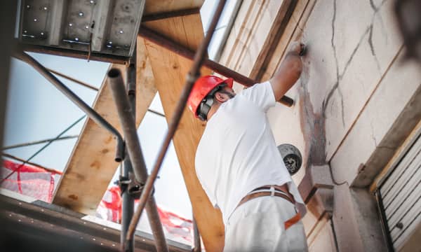 Ansicht eines Handwerkers mit weißer Kleidung und rotem Helm, der an einer Fassade arbeitet