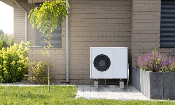 Weiße Luft-Wärmepumpe vor Hausfassade mit braunen Ziegeln