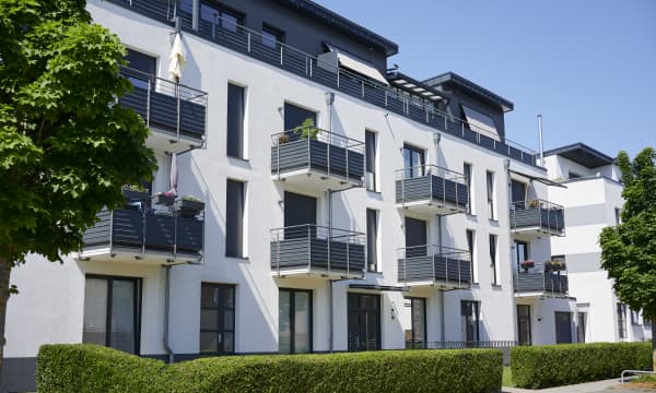 Modernes Mehrfamilienhaus mit weißer Fassade und Balkonen, davor eine gepflegte, grüne Hecke