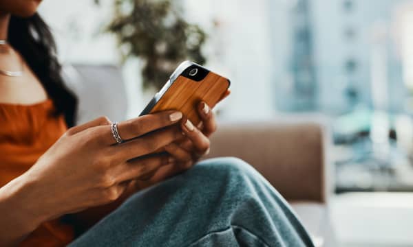 Junge Frau mit Smartphone in der Hand sitzt in Wohnung