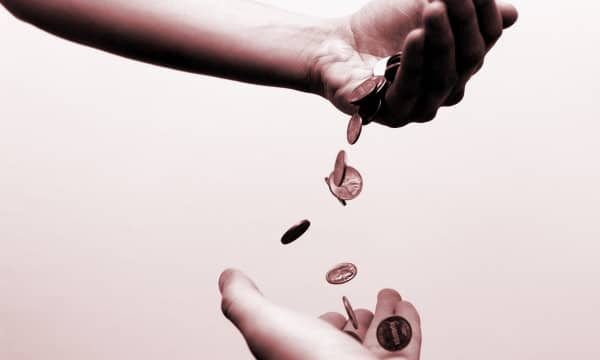 Eine Hand vor rosa Hintergrund schüttet Münzen in eine Hand unter ihr