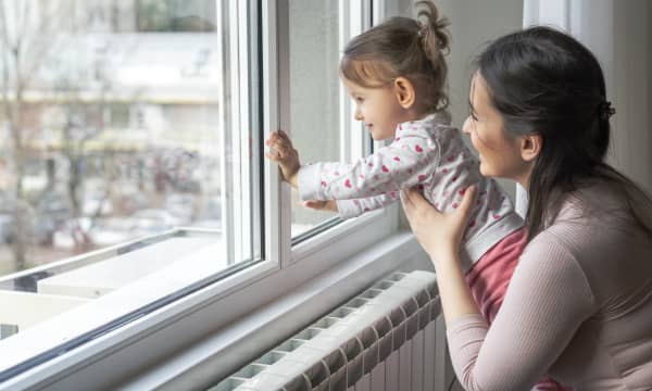 Mutter und Kleinkind schauen aus einem Fenster in einer Wohnung