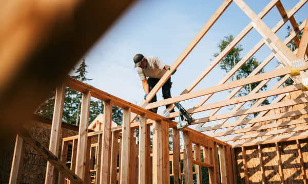 Mann auf dem Dachstuhl eines Rohbaus in Holzbauweise