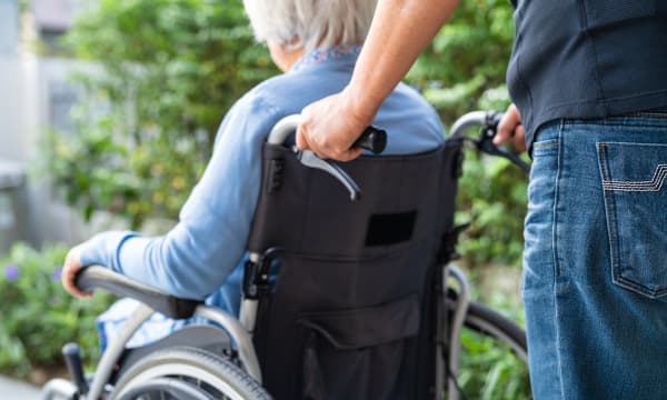 Rückansicht eines jüngeren Mannes, der eine Seniorin in einem Rollstuhl schiebt