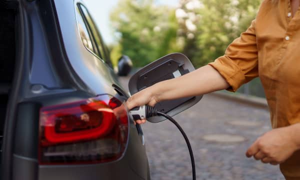Person in brauner Bluse steckt Ladekabel in ein schwarzes Elektroauto
